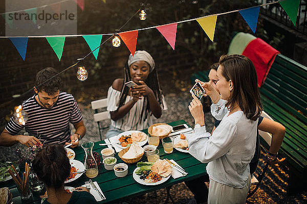 Hochwinkelaufnahme von jungen Frauen  die Freunde beim Essen während einer Dinnerparty im Hinterhof fotografieren