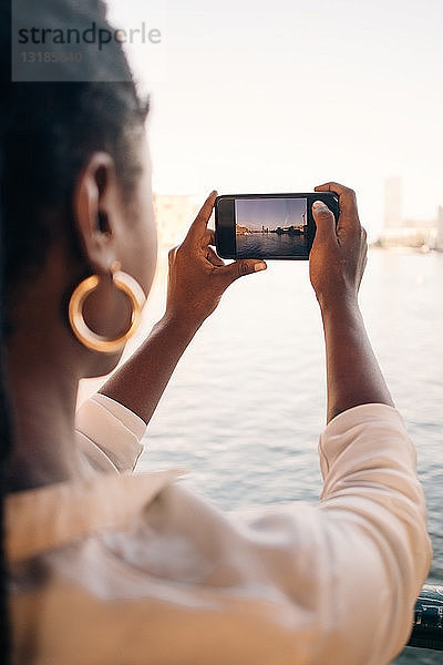 Ausschnitt einer jungen Frau  die mit einem Smartphone in der Stadt einen Fluss fotografiert
