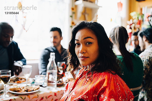 Porträt einer selbstbewussten jungen Frau  die am Tisch gegen multi-ethnische Freunde sitzt  die im Restaurant brunchen