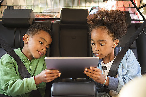 Geschwister teilen sich ein digitales Tablet  während sie in einem Elektroauto sitzen