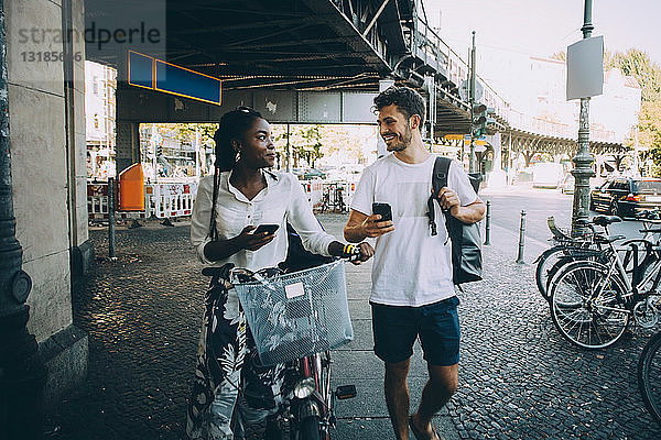 Lächelnde multiethnische Freunde unterhalten sich beim Gehen auf dem Bürgersteig in der Stadt