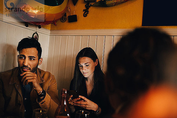Junge Frau benutzt ein Smartphone  während sie im Restaurant neben einem Mann sitzt