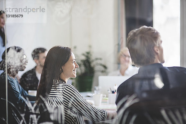 Lächelnde Geschäftsleute hören zu  während sie während des Brainstormings im Sitzungssaal sitzen