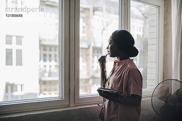 Junge Geschäftsfrau spricht durch Kopfhörer  während sie in einem kreativen Büro am Fenster steht