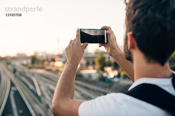 Junger Mann fotografiert per Smartphone über Eisenbahnschienen in der Stadt