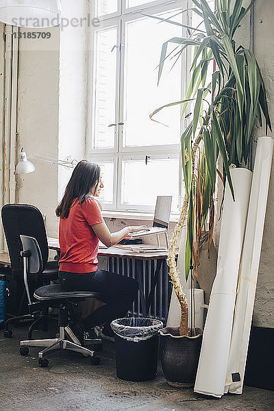 Seitenansicht einer Geschäftsfrau mit Laptop am Schreibtisch im Kreativbüro