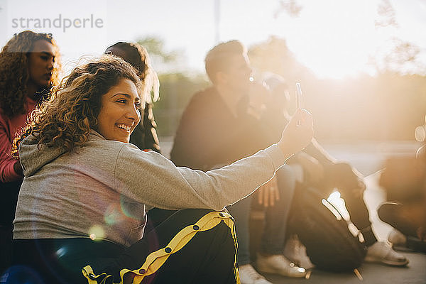 Glückliche Frau  die mit einem Smartphone Selbsthilfe betreibt  während sie mit Freunden im Park sitzt