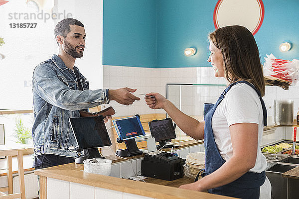 Junge Besitzerin gibt einem männlichen Kunden an der Kasse im Restaurant eine Kreditkarte