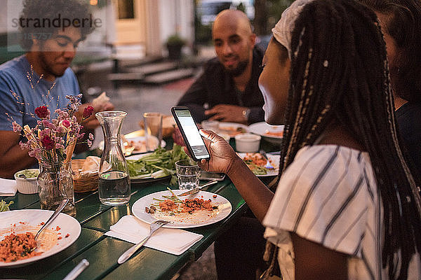 Junge Frau benutzt Smartphone beim Abendessen mit Freunden während einer Gartenparty