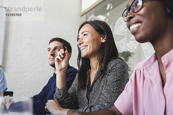 Lächelnde kreative Geschäftsleute hören zu  während sie während der Sitzung im Sitzungssaal sitzen