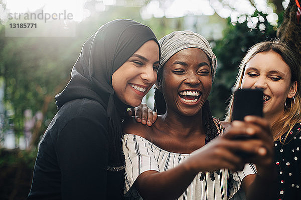Lächelnde multiethnische Freundinnen  die sich im Hinterhof per Mobiltelefon selbstständig machen
