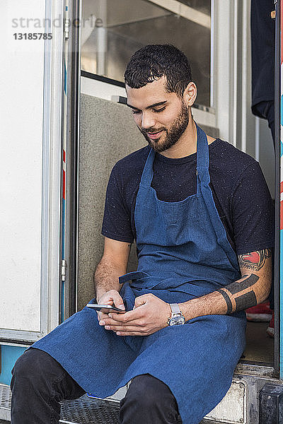 Junger männlicher Unternehmer verschickt Textnachrichten  während er am Eingang eines Speisewagens sitzt