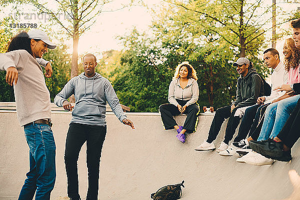 Freunde schauen Männern beim Tanzen im Skateboard-Park zu