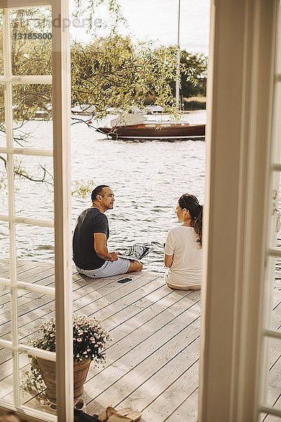 Älteres Ehepaar unterhält sich während der Arbeit auf der Terrasse  gesehen durch die offene Tür einer Ferienvilla