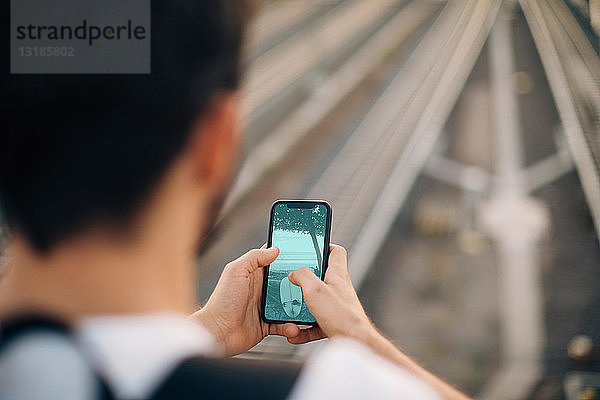 Ausgeschnittenes Bild eines jungen Mannes  der ein Smartphone über Eisenbahnschienen in der Stadt benutzt