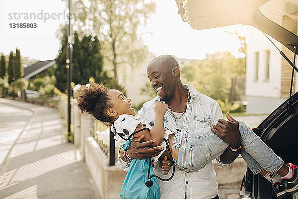 Fröhlicher Mann trägt Tochter mit Elektroauto auf Einfahrt