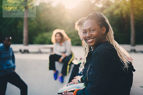 Porträt eines lächelnden Teenagers  der mit Freunden im Skateboard-Park sitzt