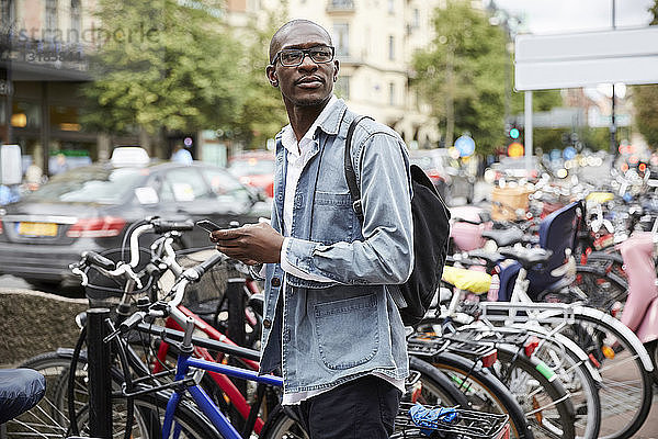 Mittlerer erwachsener Geschäftsmann schaut weg  während er in der Stadt an den Fahrrädern steht