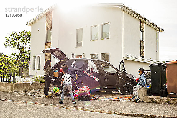 Familie mit Elektroauto auf Einfahrt gegen Haus