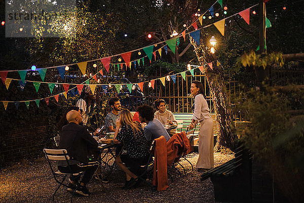 Multi-ethnische Freunde und Freundinnen genießen Dinnerparty im beleuchteten Hinterhof
