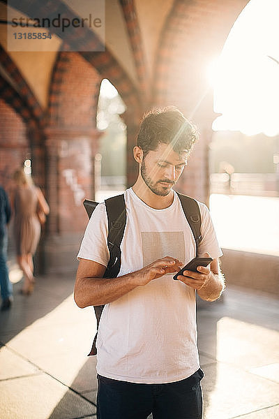 Junger Mann benutzt Smartphone  während er auf einem Fußweg in der Stadt steht