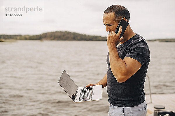 Erwachsener Mann telefoniert mit dem Laptop am See