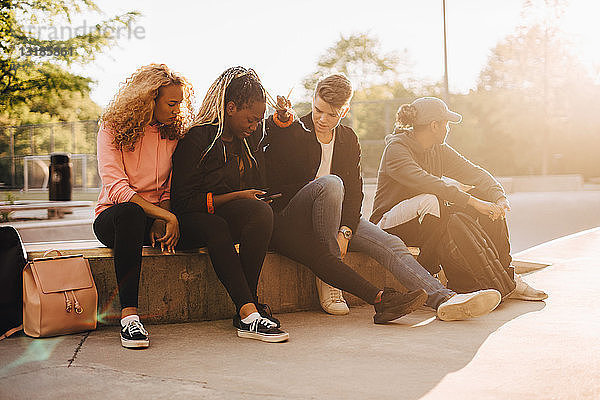 Multiethnische Freunde schauen auf Smartphone  während sie im Skateboard-Park sitzen