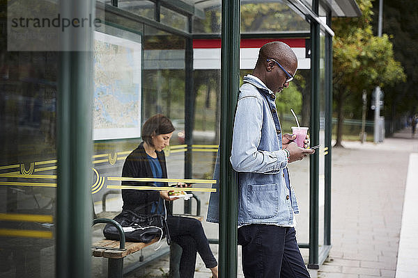 Mittlere erwachsene Pendler  die an einer Bushaltestelle in der Stadt warten