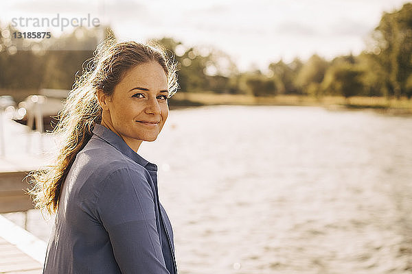 Porträt einer lächelnden  mittelgroßen erwachsenen Frau am See während eines sonnigen Tages