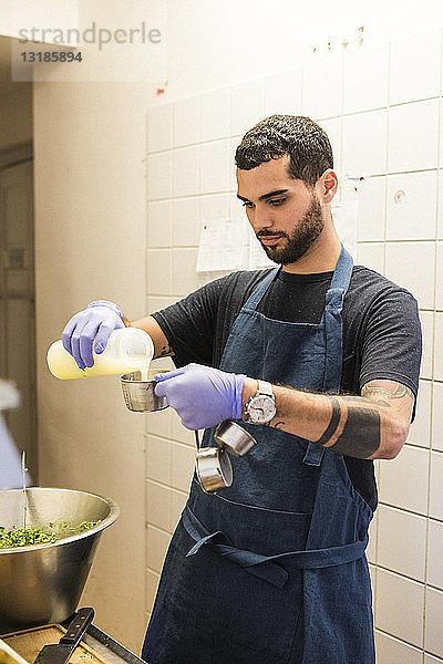 Selbstbewusster junger männlicher Koch gießt in der Großküche eines Restaurants Zutaten in einen Behälter