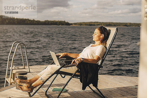 Eine Frau in voller Länge entspannt sich auf einem Liegestuhl am Steg über dem See