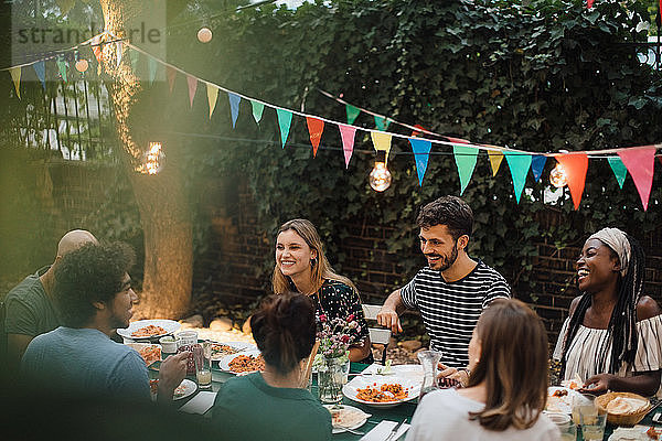Junge multiethnische Freunde genießen das Abendessen bei Tisch während einer Gartenparty