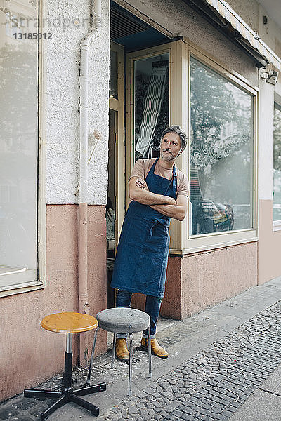 Männlicher Polsterer in voller Länge mit verschränkten Armen am Eingang der Werkstatt stehend