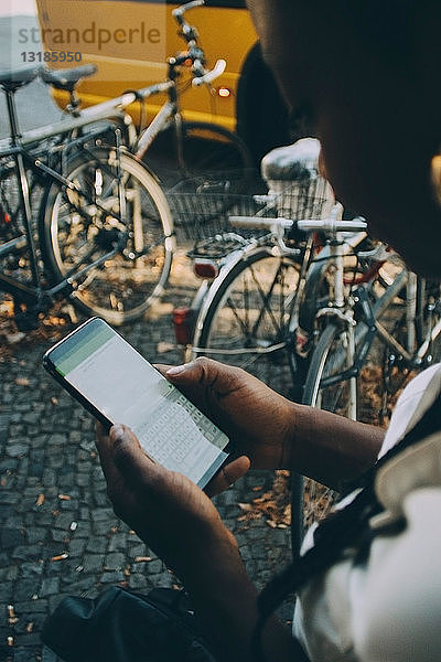 Junge Frau  die in der Stadt auf dem Bürgersteig stehend Textnachrichten per Handy verschickt