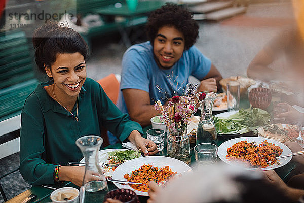 Lächelnde junge Frau schaut weg  während sie während einer Gartenparty mit einem männlichen Freund zu Abend isst