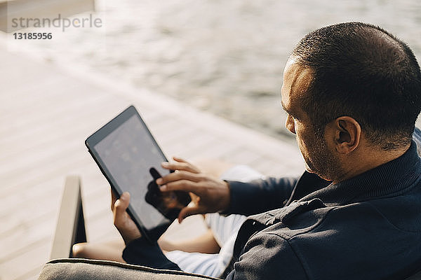 Hochwinkelansicht eines Mannes mit digitalem Tablett auf der Terrasse am See