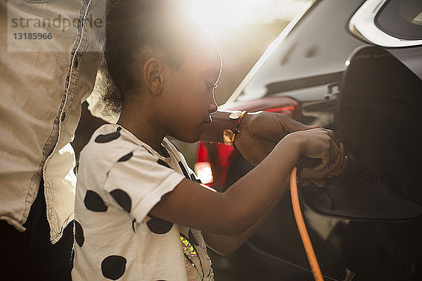 Mittelsektion eines Mannes  der seiner Tochter beim Aufladen eines Elektroautos in der Einfahrt hilft