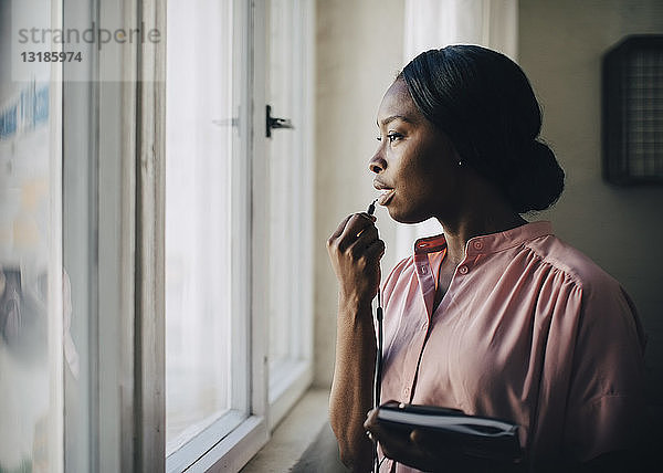 Kreative Geschäftsfrau  die durch Kopfhörer spricht  während sie im Büro am Fenster steht