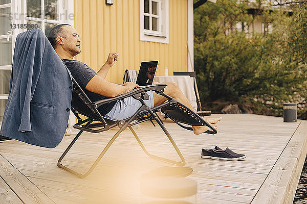 Nachdenklicher  reifer Mann mit Laptop sitzt im Innenhof einer Ferienvilla