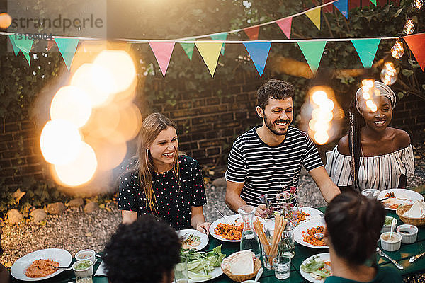 Glückliche multiethnische Freunde genießen das Abendessen am Tisch während der Gartenparty