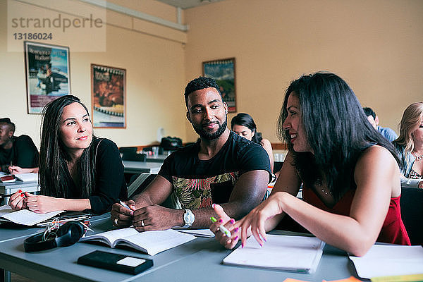 Multi-ethnische Freunde unterhalten sich am Schreibtisch im Klassenzimmer