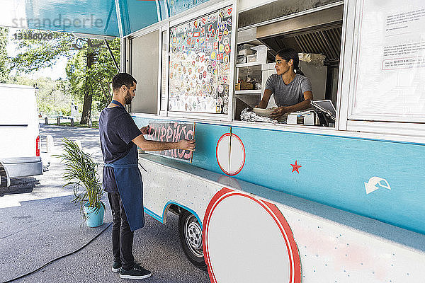 Junge männliche Besitzer kleben Poster in voller Länge auf Lebensmittelwagen in der Stadt
