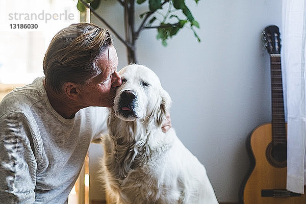 Liebender älterer Mann küsst zärtlichen Hund zu Hause