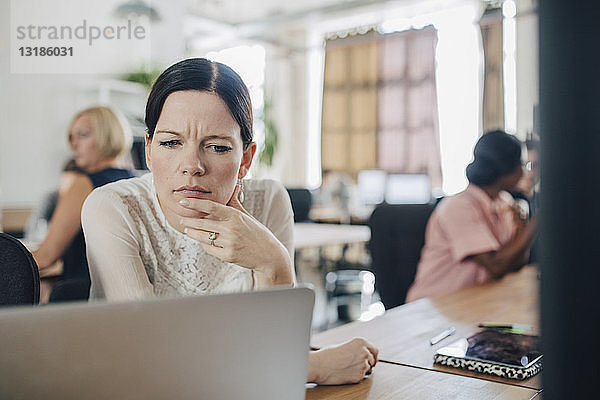 Verwirrte Geschäftsfrau schaut auf den Laptop  während sie im Kreativbüro am Schreibtisch sitzt