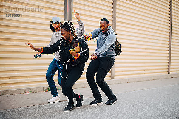 Freunde in voller Länge tanzen in der Stadt auf dem Bürgersteig vor dem Fensterladen
