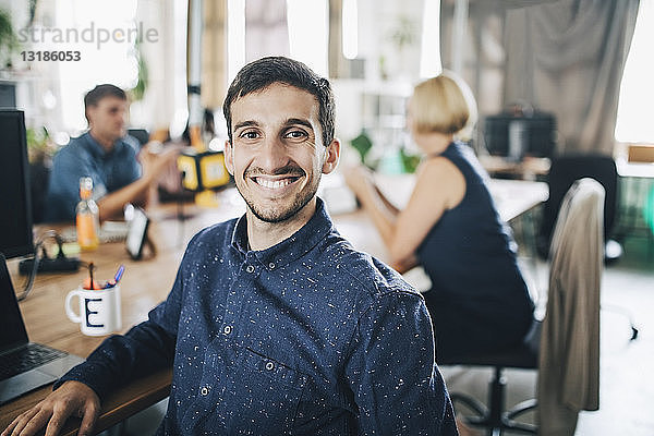 Porträt eines lächelnden jungen Geschäftsmannes  der am Schreibtisch in einem kreativen Büro sitzt