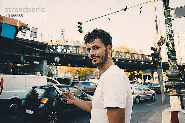 Porträt eines jungen Mannes mit einem Mobiltelefon in der Hand  der auf dem Bürgersteig in der Stadt steht