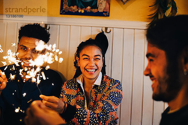 Fröhliche junge multi-ethnische Freunde sitzen mit brennenden Wunderkerzen im Restaurant