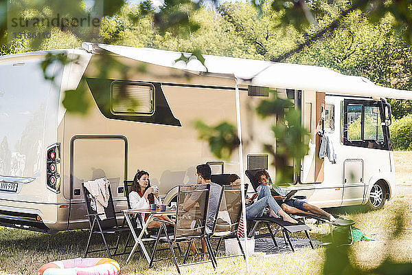 Familie entspannt sich während der Sommerferien auf Stühlen vor dem Wohnmobil auf dem Campingplatz