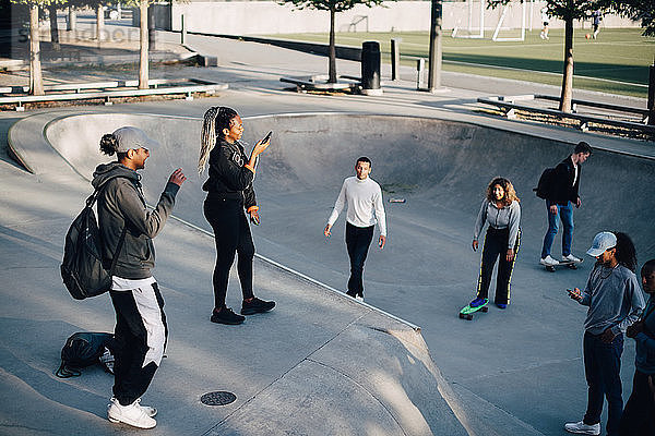 Schrägansicht von Freunden beim Mobiltelefonieren und Skateboarden im Park
